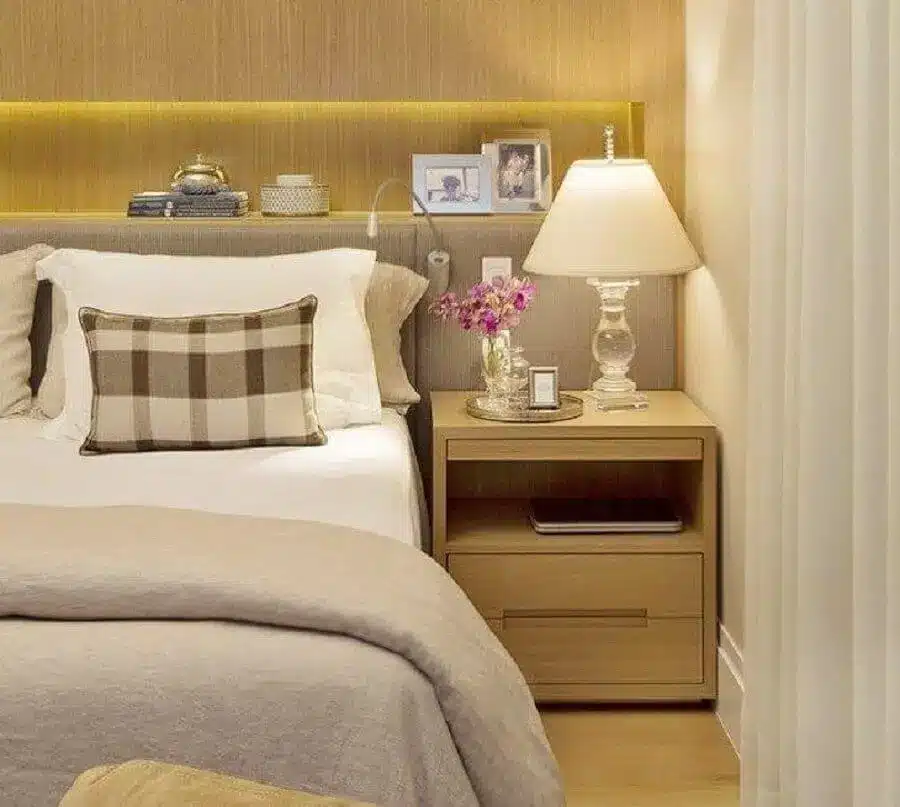 Decoração com criado mudo de madeira e abajur para quarto de casal com base de vidro.