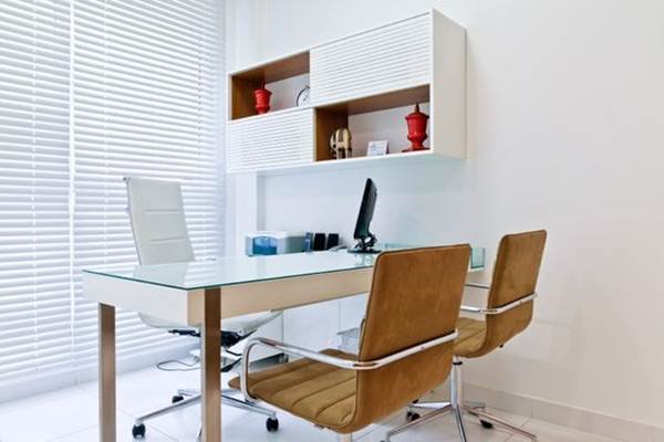 A smaller environment also pairs well with more streamlined and neutral décor. The small office features white and caramel-colored chairs, white blinds, and a suspended cabinet with red decorative items that stand out.