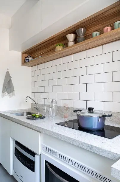 Granite sink: wall covered in white brick, granite countertop, white wooden furniture, built-in cooktop, and wooden niche – Project: Gabriela Toledo