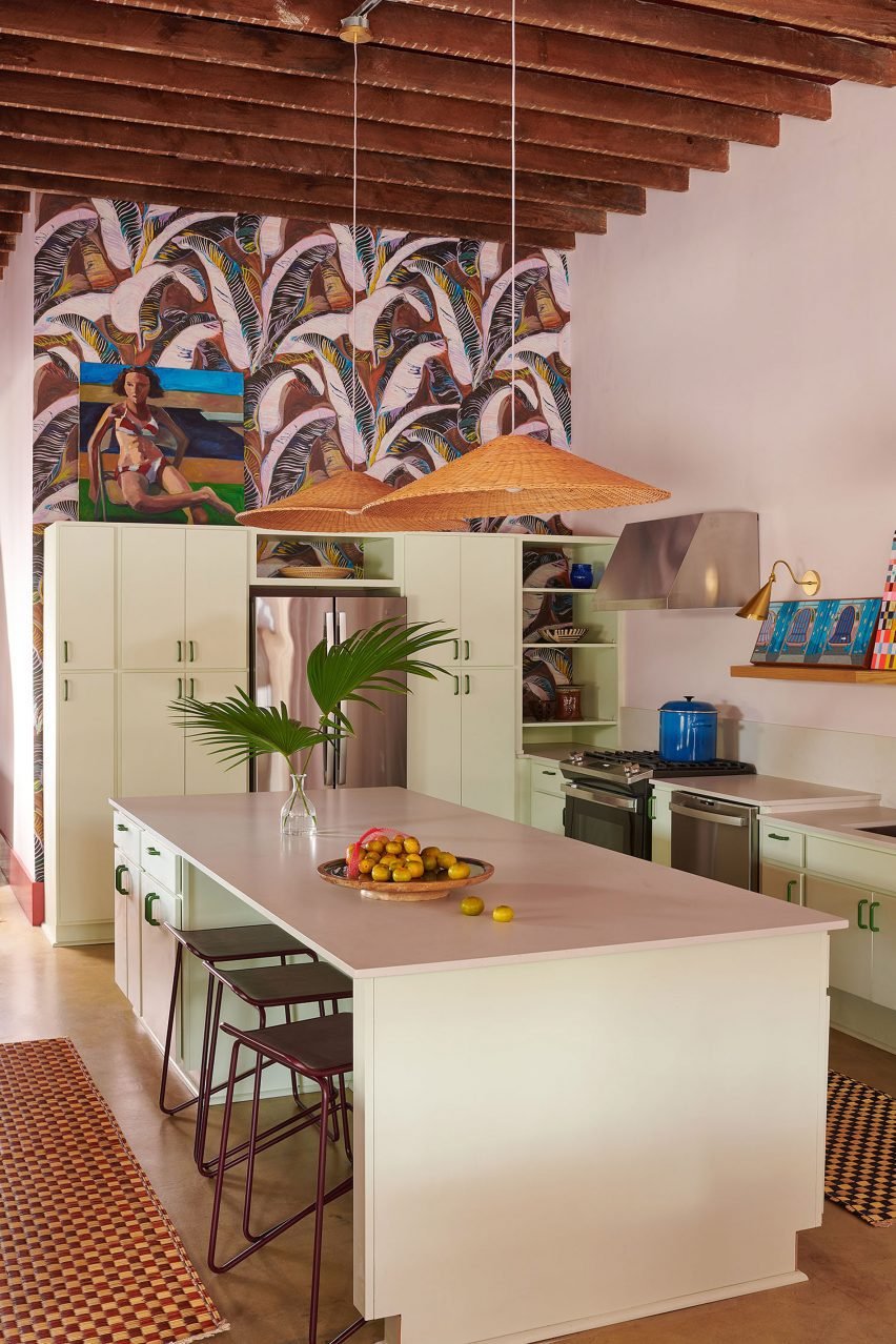 Os armários da cozinha são verdes e a papel de parede retrata o clima tropical.