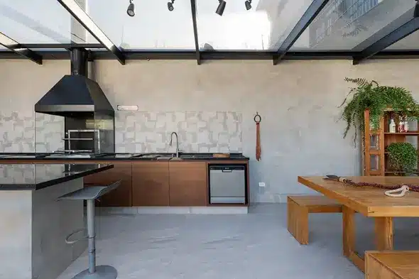 Imagem que combina móveis de madeira, churrasqueira de vidro e eletrodomésticos inox em uma área de churrasco.