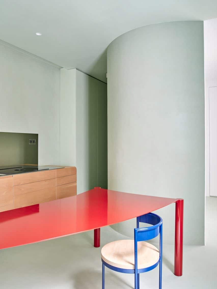 Crimson dining table contrasting with pale sage-green kitchen.