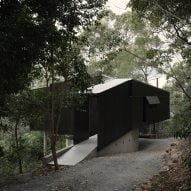 Imagem da casa negra projetada por Fouché Architects em um bosque.