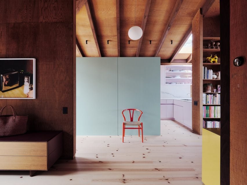 Minty green storage unit alongside a baby pink kitchen in a timber-heavy interior.